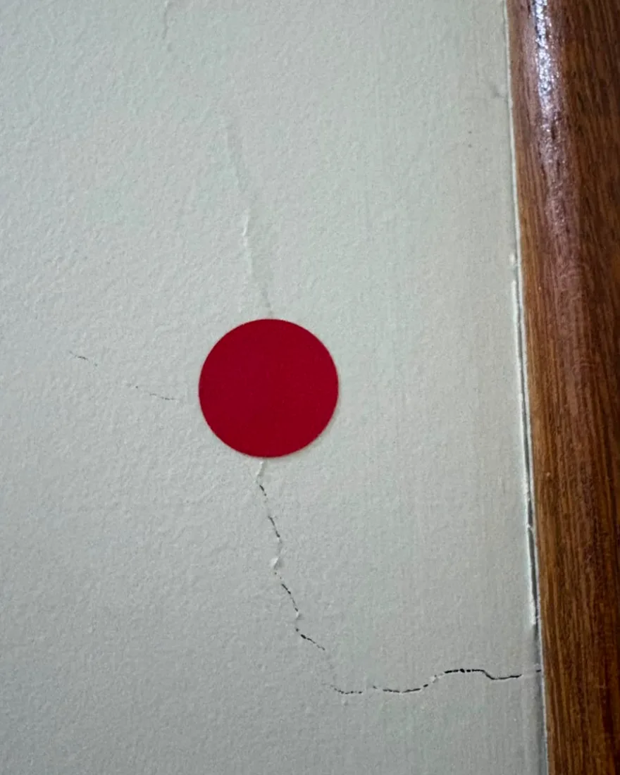 Fissura em parede descendo até o batente de madeira da porta, marcada com adesivo vermelho