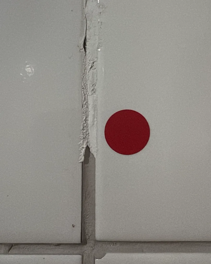 Faixa de massa corrida aplicada entre placas cerâmicas no lugar do revestimento, marcada com adesivo vermelho