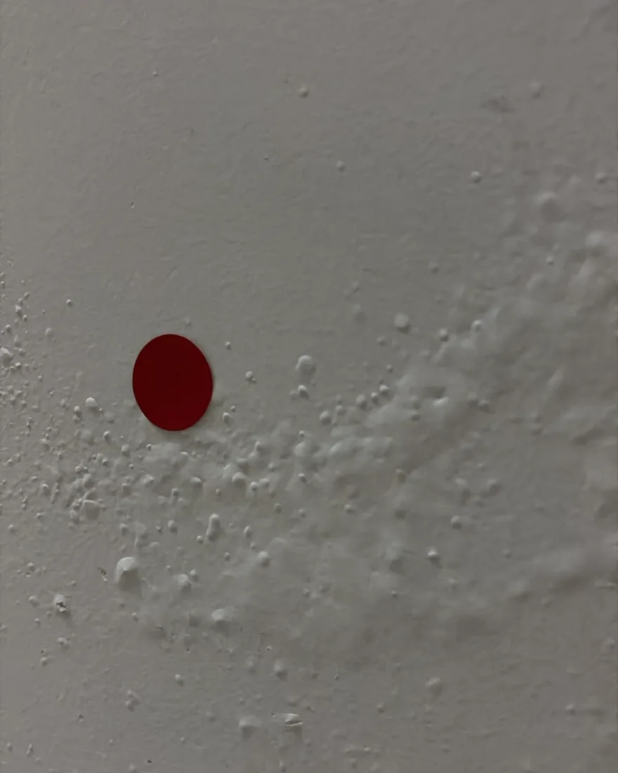Bolhas e descolamento de pintura na base de uma parede, marcados com adesivo vermelho